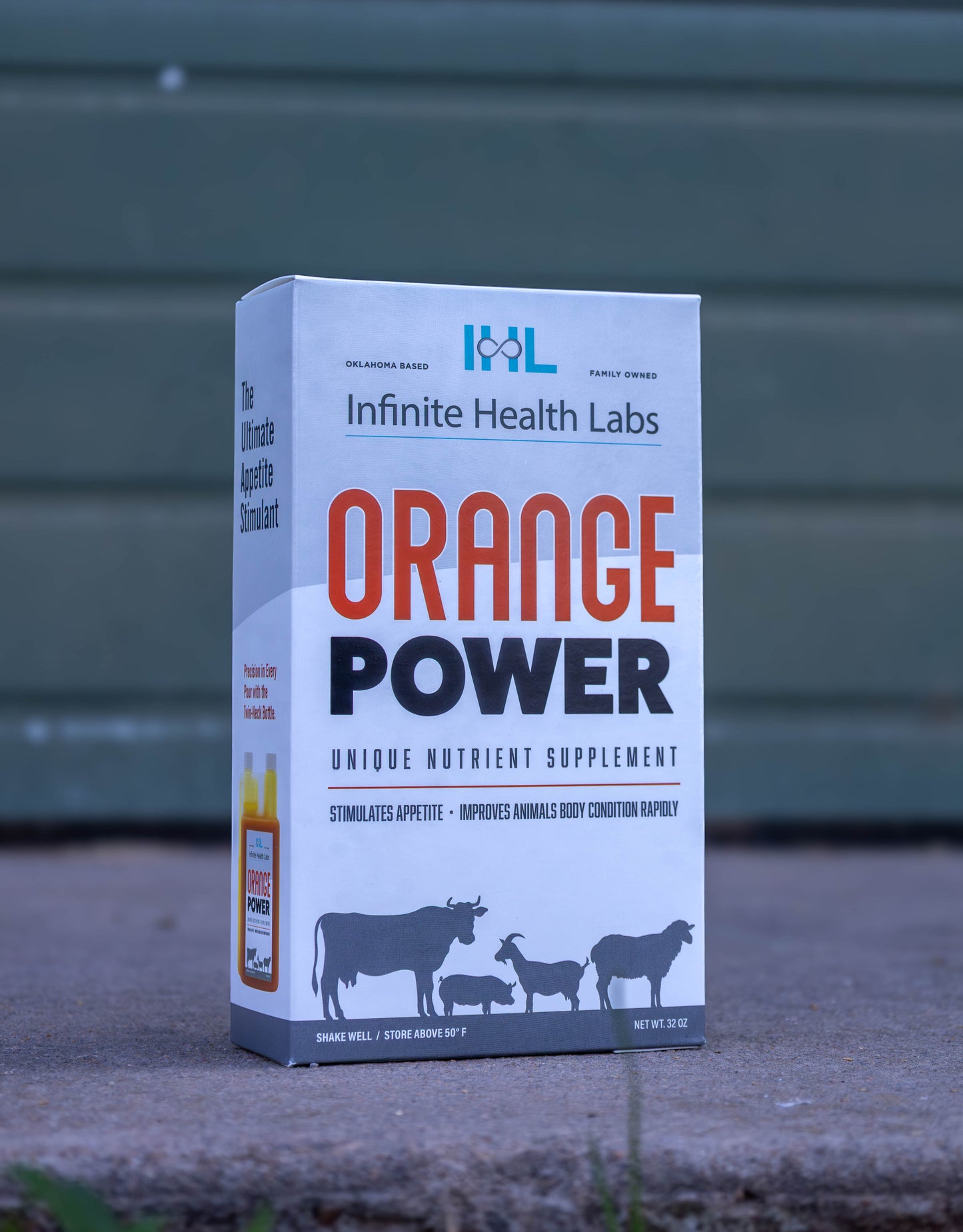 A box of Infinite Health Labs Orange Power liquid supplement for livestock stands on a surface, showing cow, pig, sheep, and goat illustrations and text highlighting it as an appetite stimulant for show animals.