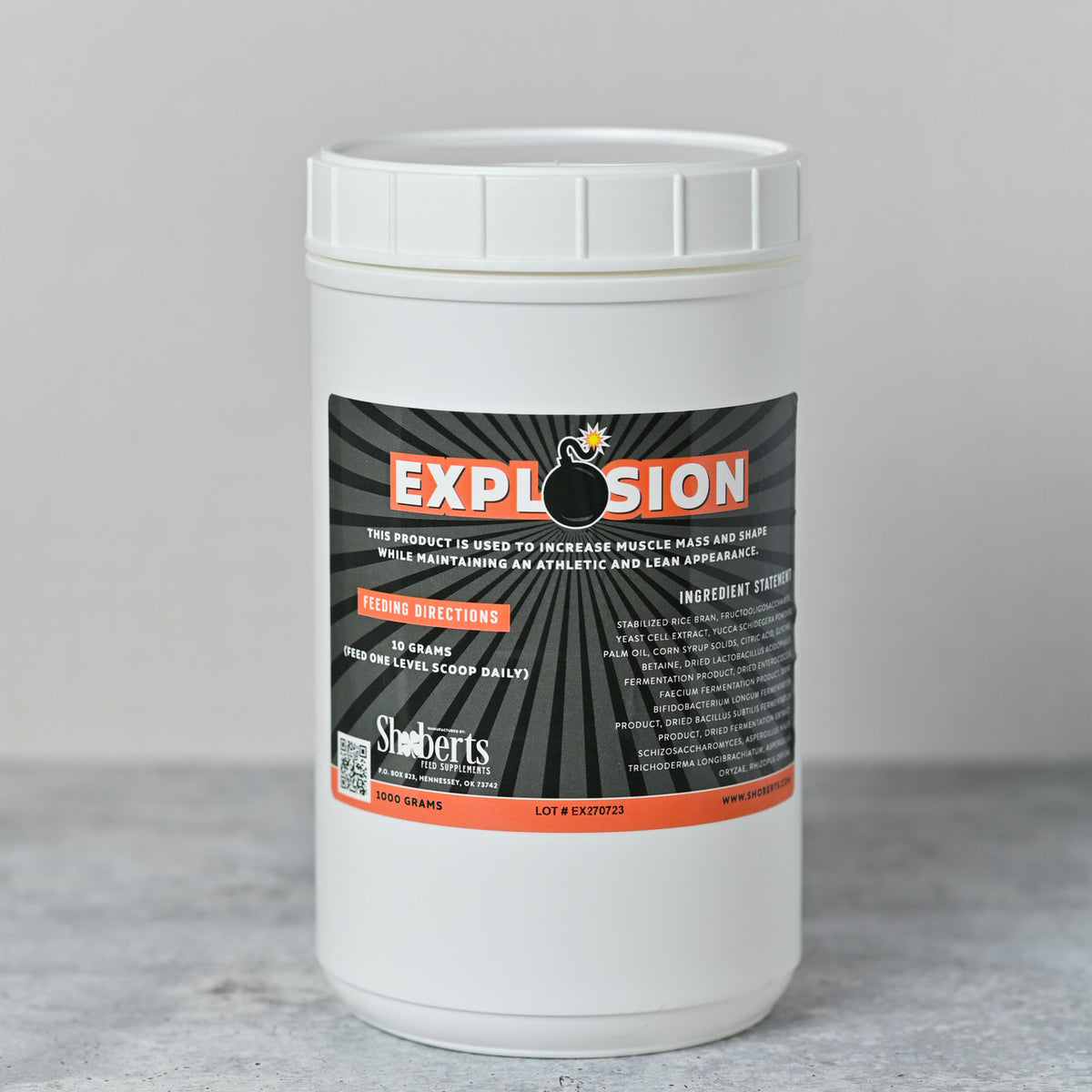 A white container of Infinite Health Labs’ Explosion Livestock Supplement—featuring bold orange and black text on the label—sits atop a gray surface. The packaging displays feeding directions and ingredient information, emphasizing its use as a supplement designed to support muscle growth, shape, and density in show animals.
